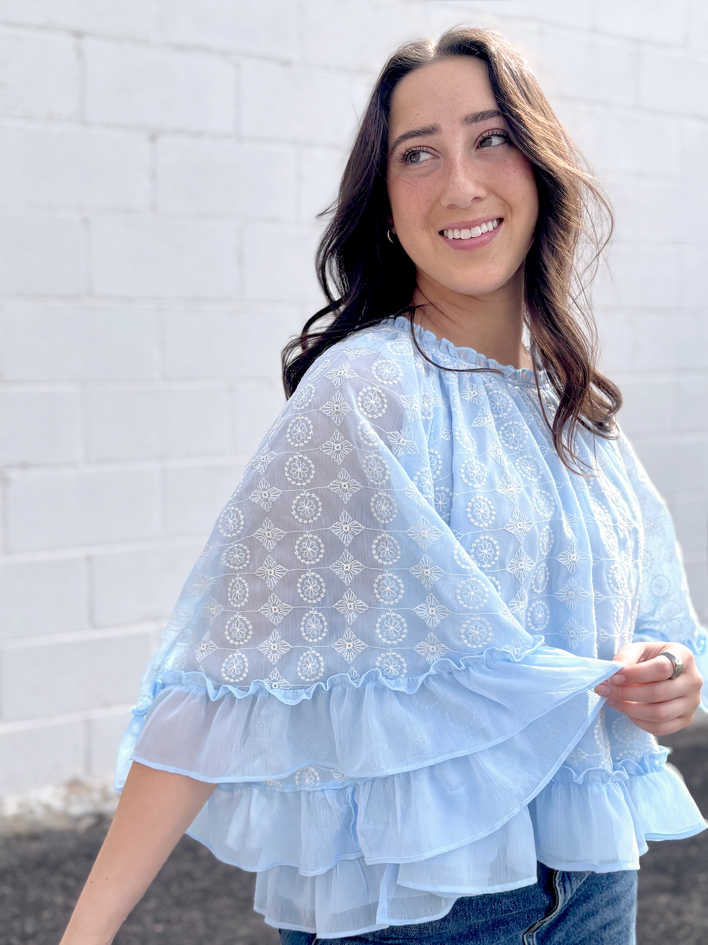 Light blue cape top with white embroidered pattern over top and ruffles along the sleeves and bottom of top
