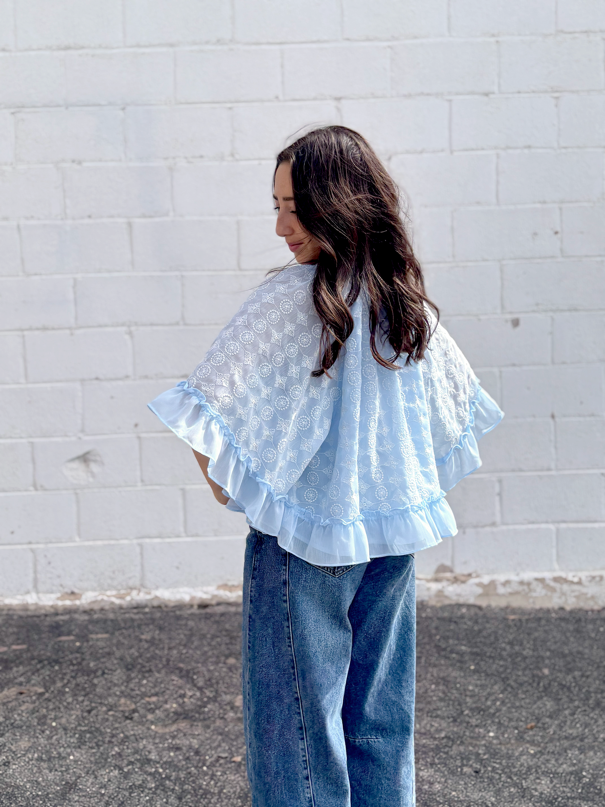 Light blue cape top with white embroidered pattern over top and ruffles along the sleeves and bottom of top