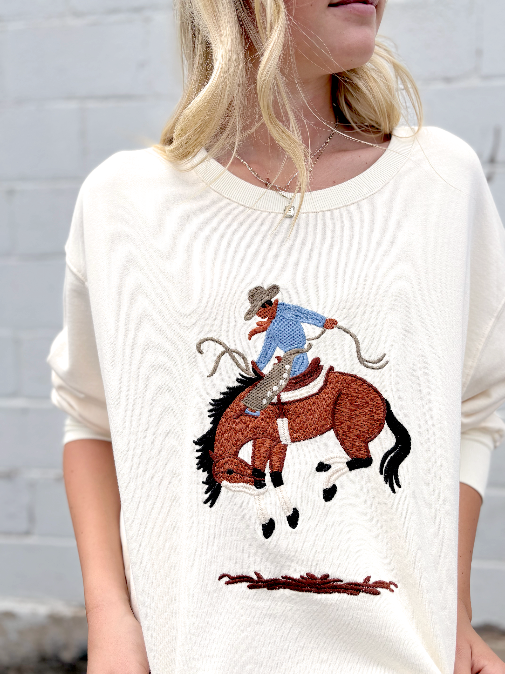 Cream colored sweater with a cowboy embroidered on the front