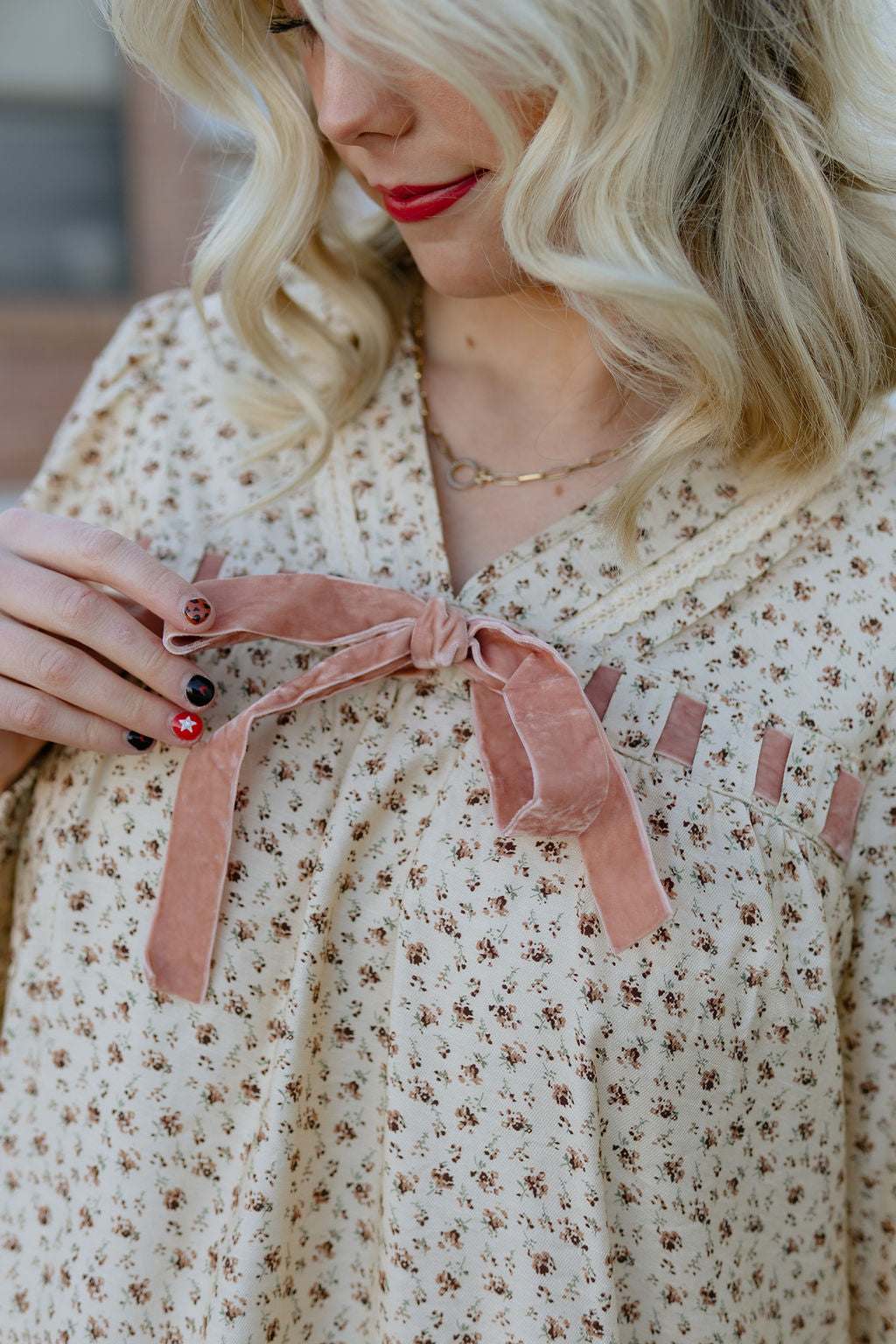 Beige babydoll dress with dark red floral pattern; long in the back and short in the front with velvet bow along neckline